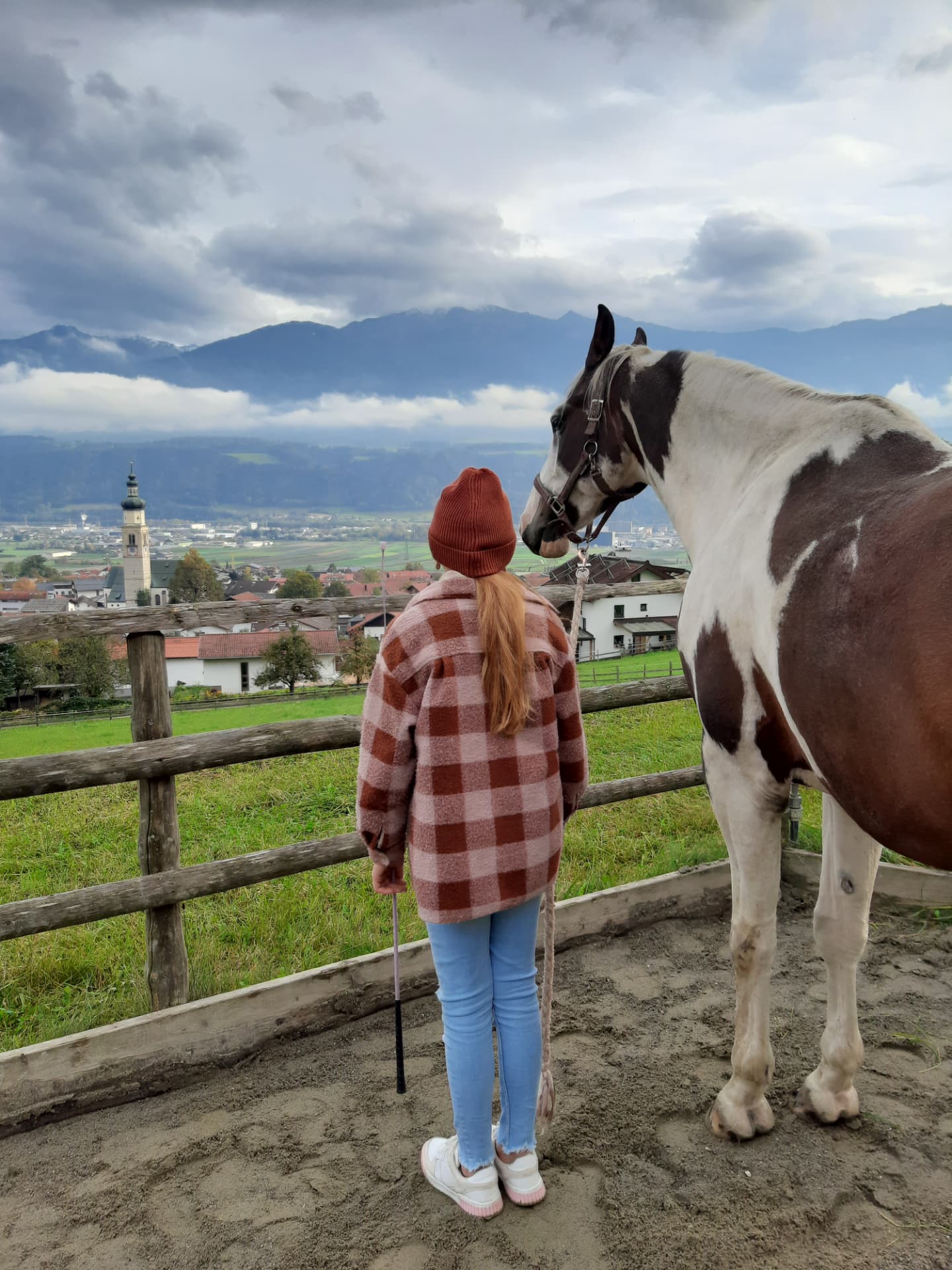 Mädchen steht mit einem gescheckten Pferd vor dem Blick ins Tiroler Tal