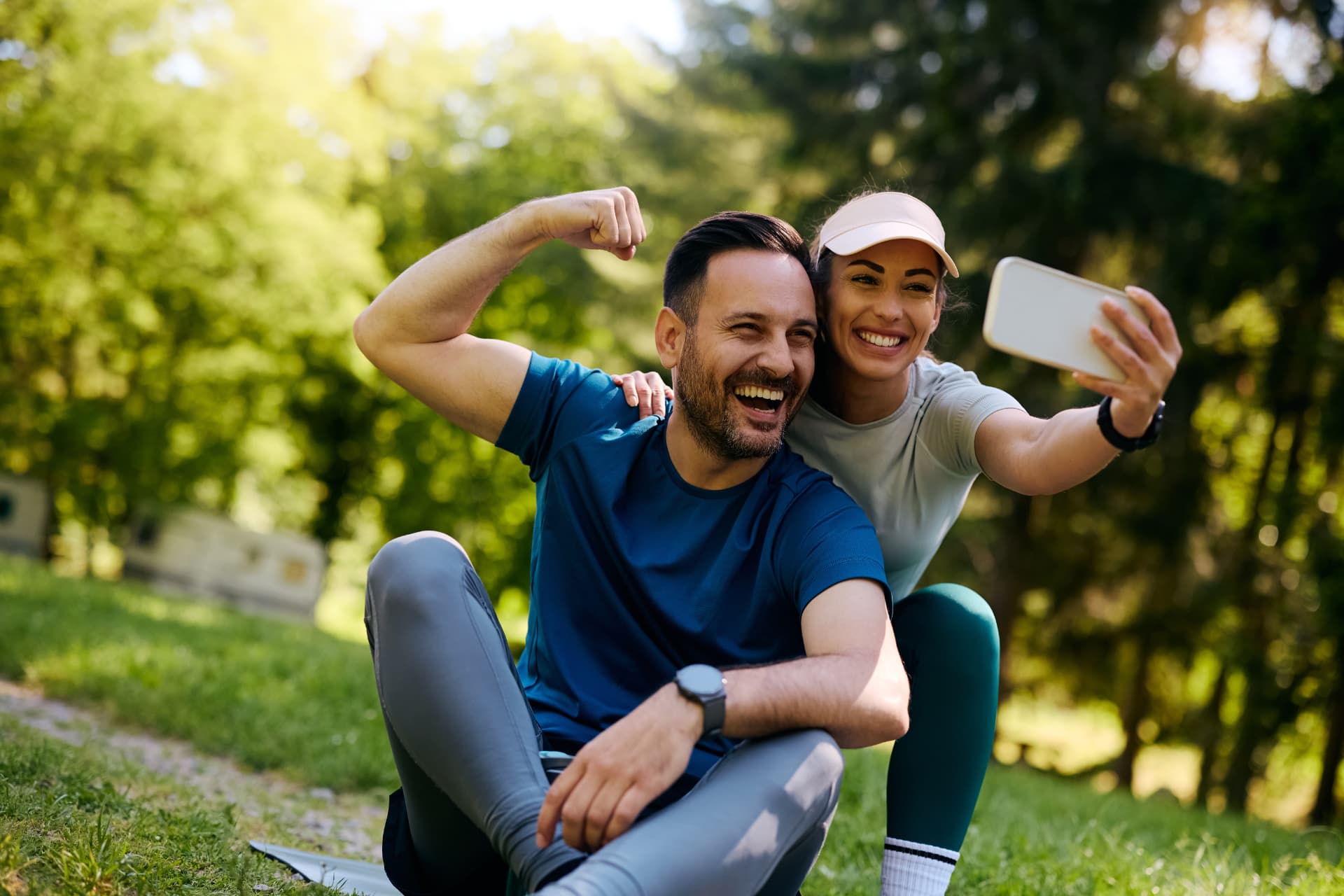 Sportliches Paar sitzt lachend im Grünen und macht ein Selfie